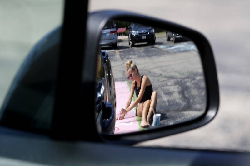 Emma Weber, is reflected in a cars mirror as ehe helps her sister, Tessa, paint hearts on Tessa’s parking spot on Tuesday, Aug. 13, 2024, at Marion Central Catholic High School in Woodstock.