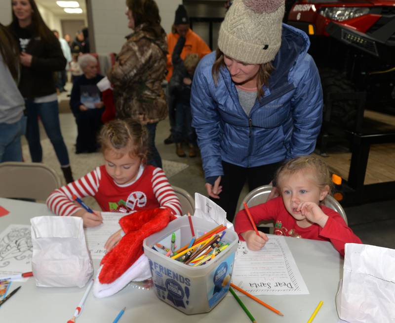 Ellie and Maci Wolf, 4 and 6, of Fulton, contemplate what to put in their letters to Santa as their mom, Carissa, helps during Erie's Hometown Holidays on Saturday, Dec. 2, 2023. Letter writing was one of the kids activities offered at the Erie Fire Station.