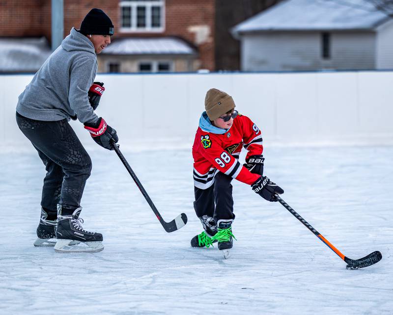 Weston Harris dribbles puck down rink as Timmy Dierks trails whilst iceskating during game of hockey at Schweickert Arena's Ice Rink on Tuesday, December 30, 2025, at Washington Park in Peru.