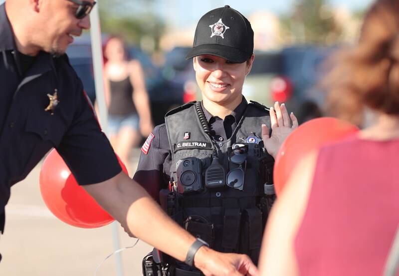 Northern Illinois University Police Detective Cori Beltran waves to kids as she hands out balloons Tuesday, Aug. 2, 2022, during National Night Out in the parking lot of the Walmart on Sycamore Road in DeKalb.