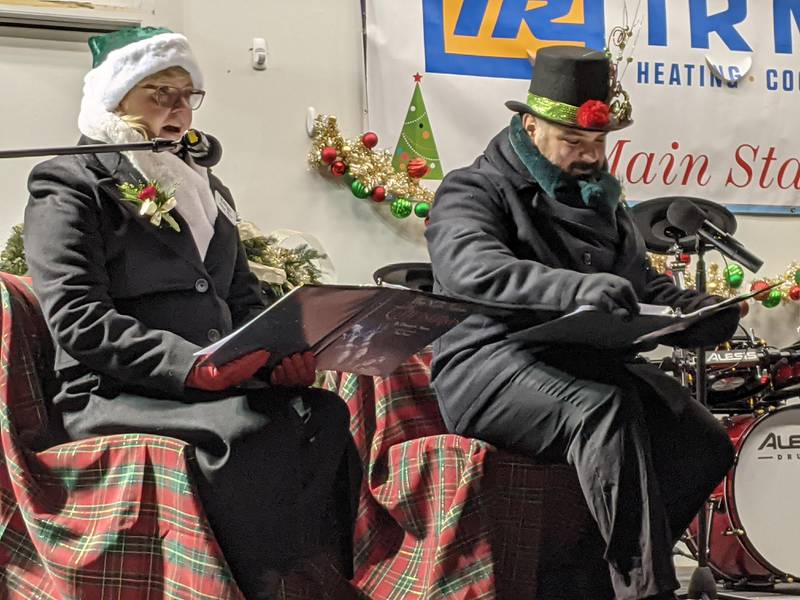 Oswego village trustees Karen Novy, left, and Andrew Torres, right, read the poem “Twas the Night Before Christmas” to those gathered in front of the main stage at the Oswego Christmas Walk on Dec. 6.