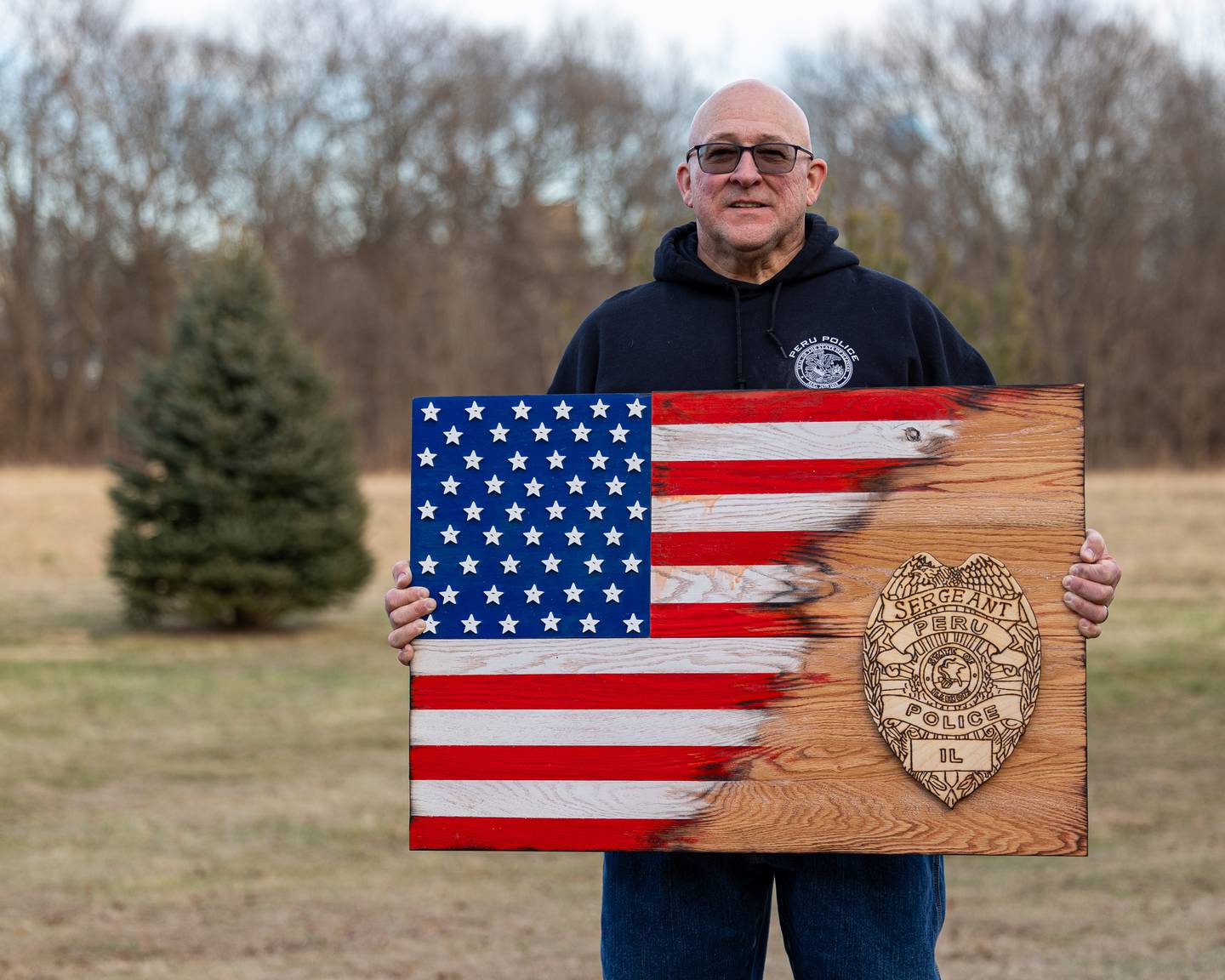 Retired Peru Police Sergeant Ed DeGroot poses for photo holding wooden art piece gifted to him by fellow Peru Police Sergeant and Brother Scott DeGroot on Monday, January 12, 2026. Sergeant DeGroot retired from the Peru police department after 30 years of service on January 2nd.
