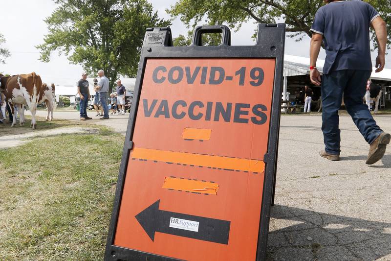 Crowds navigate the attractions around a COVID-19 vaccination sign during the McHenry County Fair at the McHenry County Fairgrounds on Friday, Aug. 6, 2021 in Woodstock.  The fair continues through Sunday.