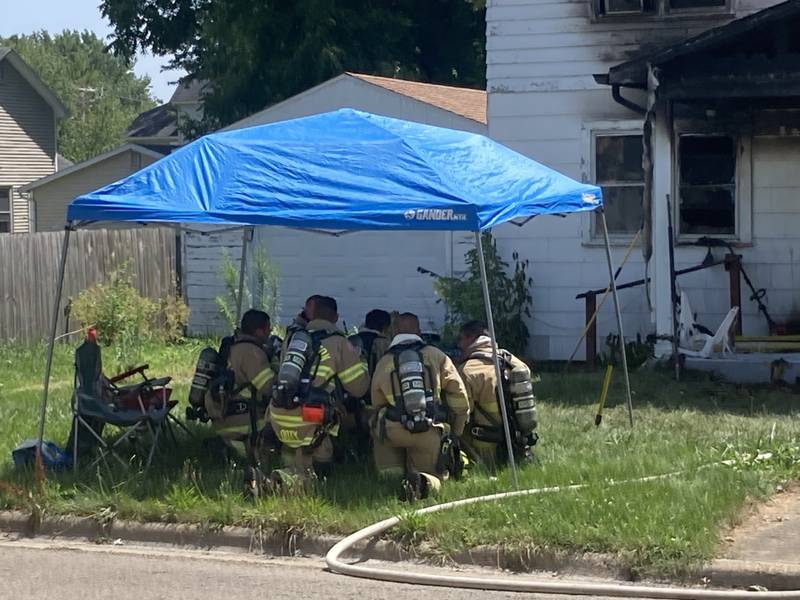 Fire fighters take some shade on a 100-degree plus heat index day after putting a residential fire out on the 200 block of West Clark St. in Princeton on Friday afternoon.