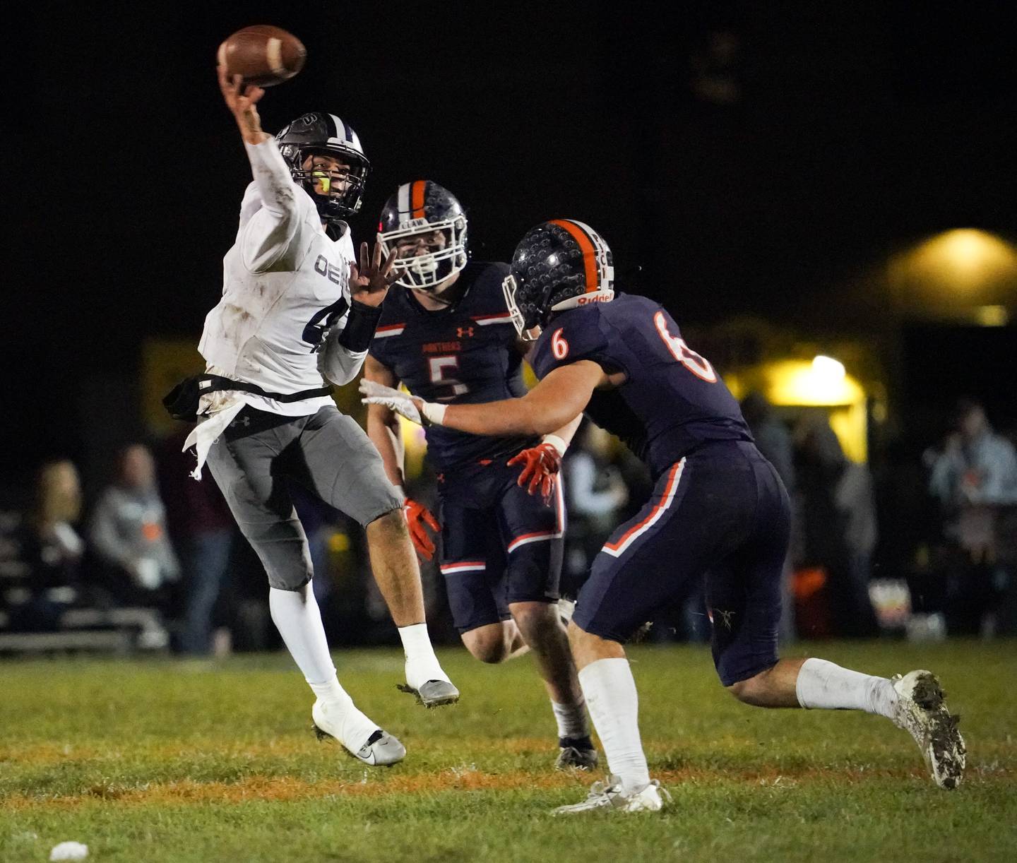 Oswego East's Niko Villacci (4) throws a pass while under pressure by Oswego’s Carson Cooney (5) and Michael Claycombe (6) during a football game at Oswego High School on Friday, Oct. 20, 2023.