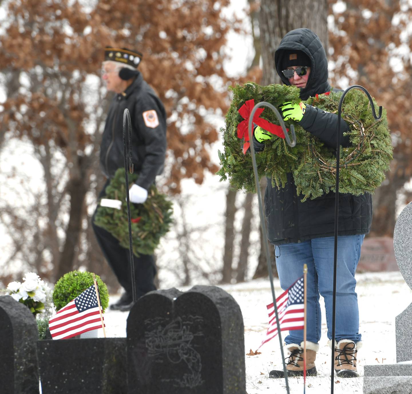 Anne Stevens of Oregpn places a wreath on a veteran's grave in Daysville Cemetery, southeast of Oregon, on Dec. 17, during the Wreaths Across America project. Stan Eden, also of Oregon, is shown in the background carrying one of the wreaths to another grave.