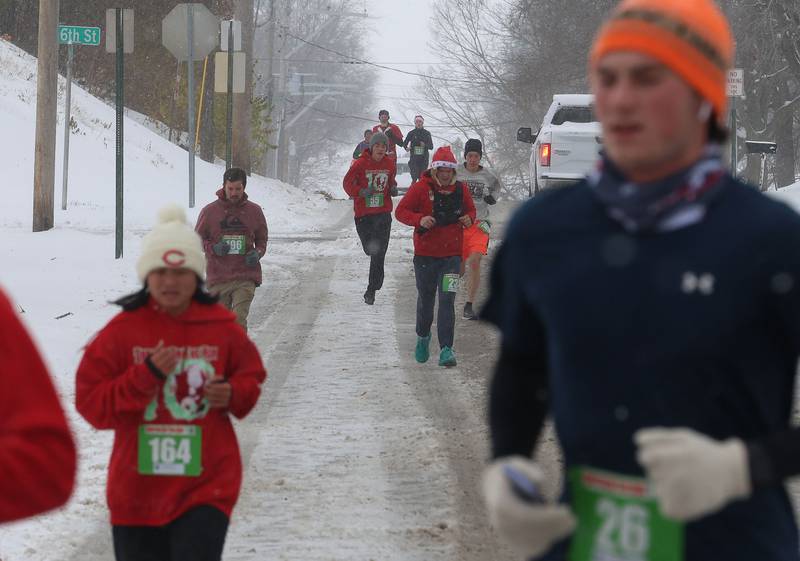 Runners brave the cold and snow while running down hill near the corner of 5th and Greenwood Street during the Santas on the Run 5K and one-mile walk on Saturday, Nov. 29, 2025 in Spring Valley.