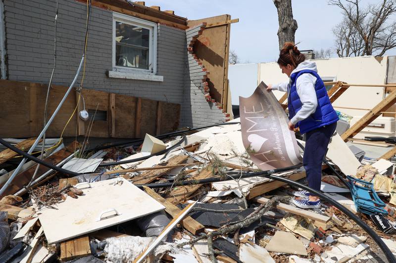 Emily LaVoie pulls a welcome mat from the debris of her Elmwood Drive home in Aroma Township on April 8, 2026. She and her husband, Dave Herberger,  are in the process of planning repairs for the damage caused by the EF-3 tornado about one month ago.