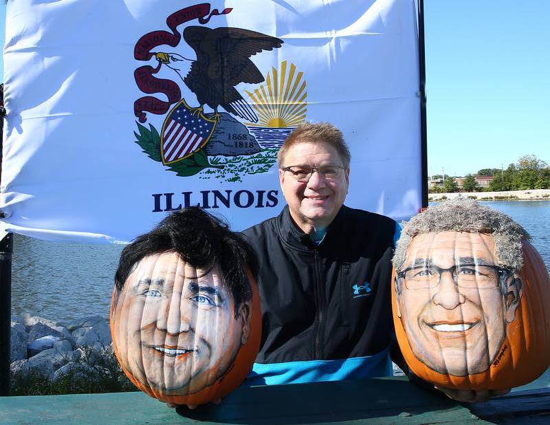 John Kettman of La Salle, poses with his pumpkins that he made of Gov. J.B. Pritzker and candidate for Gov. Darren Bailey on Wednesday, Sept. 28, 2022 at Allen Park in Ottawa. Kettman is world famous for replicating political and celebrities on the face of a pumpkin.