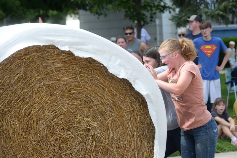 Breana West and Keandrie Marceau roll a large round straw bale down Wesley Avenue in Mt. Morris during the Straw Bale Race at Strawfest on Saturday, Aug. 23, 2025. The team with the fastest time won the event.