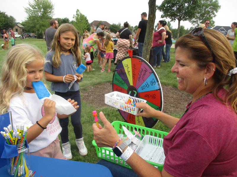 Yorkville Public Library Youth Services Director Jennette Weiss offers prizes to Lillie Pettit, 6, left, and sister Grace Pettit, 7, both students at Grande Reserve Elementary School, at the Yorkville Storywalk family event on Sept. 20.