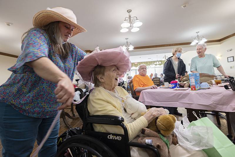 Rae Higly, resident services coordinator at Heritage Woods, gussies up Margie Mathias with a fancy hat Friday, March 31, 2023. Mathias helped plan the tea party by picking out chocolate chip cookies, ice cream and pretzels as snacks and colors, “anything bright.”