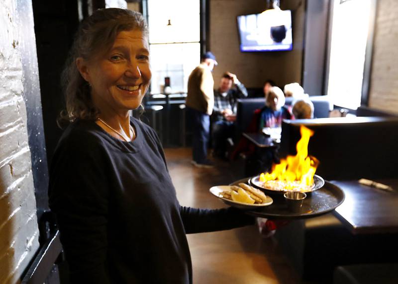 Debbie McGivern holds a plate of saganaki  on Tuesday, Nov. 12, 2024, at Squire on the Square in Woodstock. 

The restaurant, which has similar decor as other Village Squire restaurants, is a joint venture between the Linardos family and Bob Karas of Karas Restaurant Group.
Squire on the Square is located in the basement of the Old Courthouse in Woodstock, and its menu will features items similar to the Linardos family’s restaurants and the Village Squire.  

The eatery replaces the Public House that closed at the end of March.