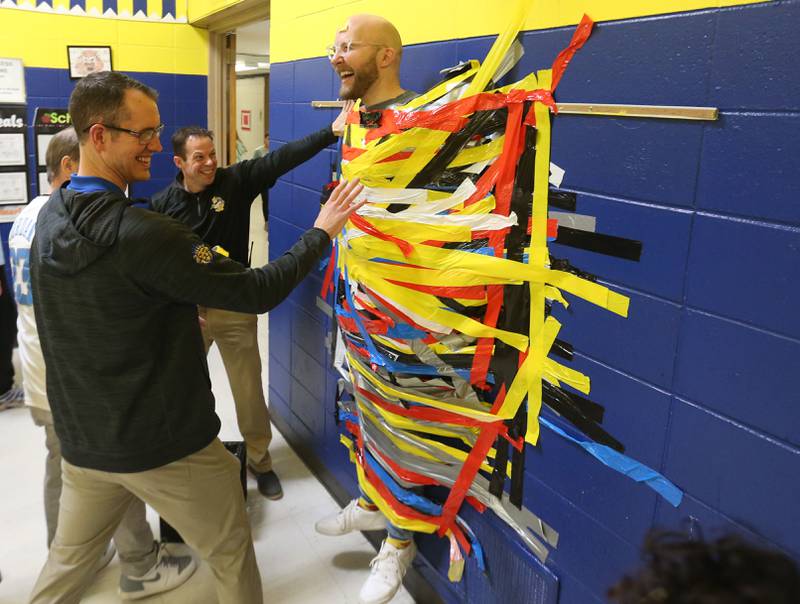 (From left) Principal Zach Smith, and assistant principal Scott Daly react as Mr. Andrew Strickler is taped to the wall during the "Tape The Teacher" fundraiser on Friday, March 20, 2026 at Logan Jr. High School in Princeton.