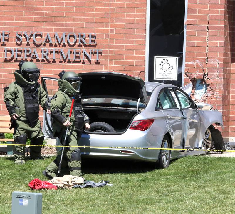 Officers in protective gear search a car Wednesday May 26, 2021, that crashed into the Sycamore Police Department on DeKalb Avenue. Law enforcement from several agencies are on hand investigating, and the cause of the crash remains unknown at this time.