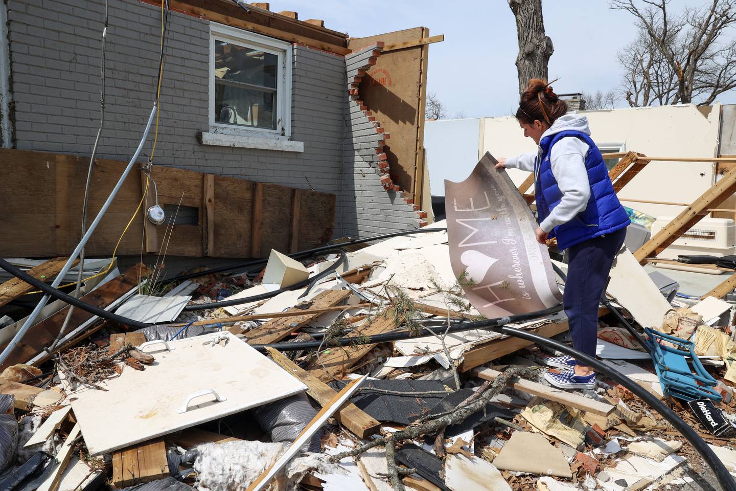 Emily LaVoie pulls a welcome mat from the debris of her Elmwood Drive home in Aroma Township on April 8, 2026. She and her husband, Dave Herberger,  are in the process of planning repairs for the damage caused by the EF-3 tornado about one month ago.