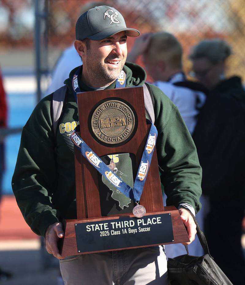 Coal City head coach Steve McCleary carries the trophy Friday, Nov. 7, 2025, after their Class 1A state third place win over Chicago Academy at Hoffman Estates High School.
