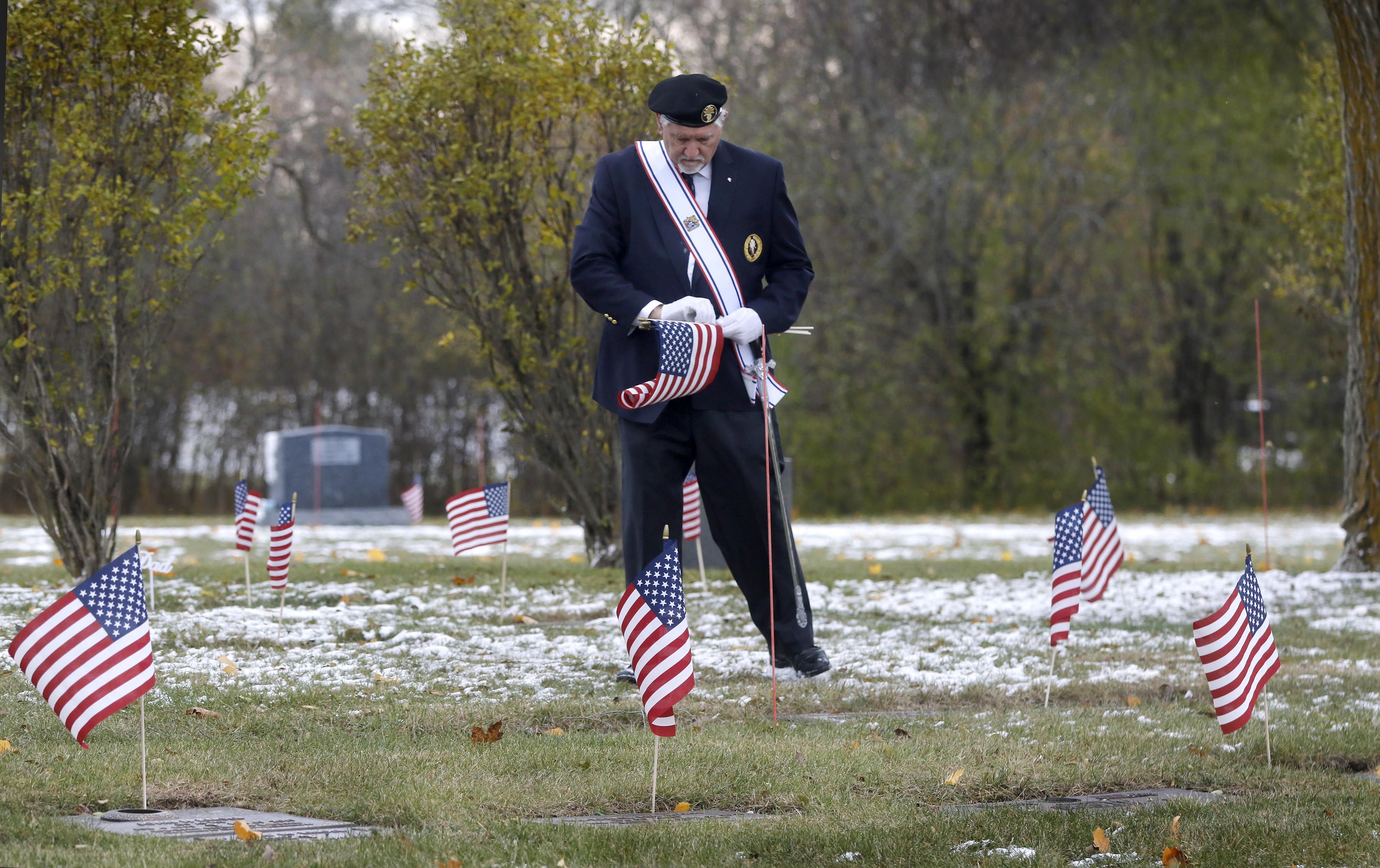 Chris Bednarek places flags during the Veterans Day flag placement ceremony Tuesday, Nov. 11, 2025, at the gravesites of veterans at McHenry County Memorial Park Cemetery in Woodstock.