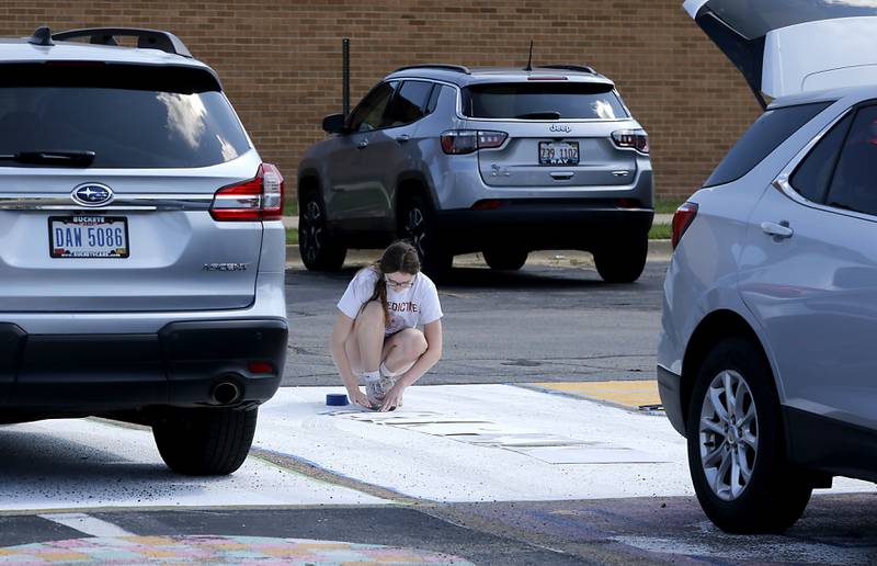 Marian Central Catholic High School senior  Juliette Huff is surrounded by parked cars as she tapes down a stencil on Tuesday, Aug. 13, 2024, before paints words on her parking spot.