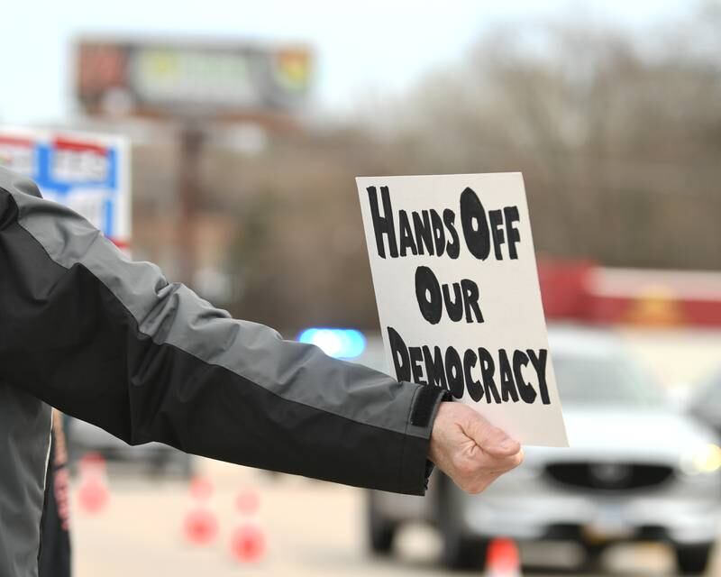 A sign reading “Hands Off our Democracy” is held during the Hands Off Demonstration on Saturday April 5, 2025, along Ogden Ave.  outside the Tessla dealership in Lisle.