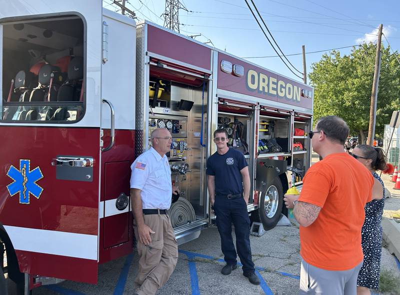 Oregon Fire Chief Michael Knoup (left) chats with visitors as he stands by an Oregon fire truck during the National Night Out event in Oregon on Tuesday, Aug. 5, 2025.