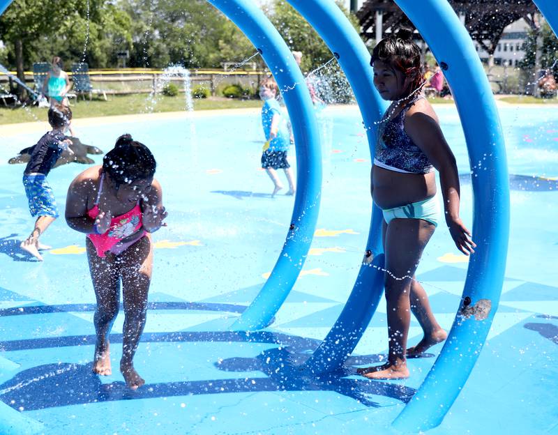 Inesmaria Medina runs through the water as her sister, Xochitl, looks on at the Westmont Park District’s Ty Warner Park splash pad on Tuesday, June 21, 2022. Temperatures were expected to reach the upper 90s.