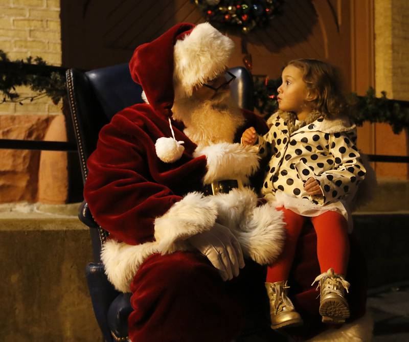Santa Claus talks with Giovanna Knudson, 2, of Crystal Lake, during the Lighting of the Square Friday, Nov. 25, 2022, in Woodstock. The annual event featured brass music, caroling, free doughnuts and cider, food trucks, festive selfie stations and shopping.
