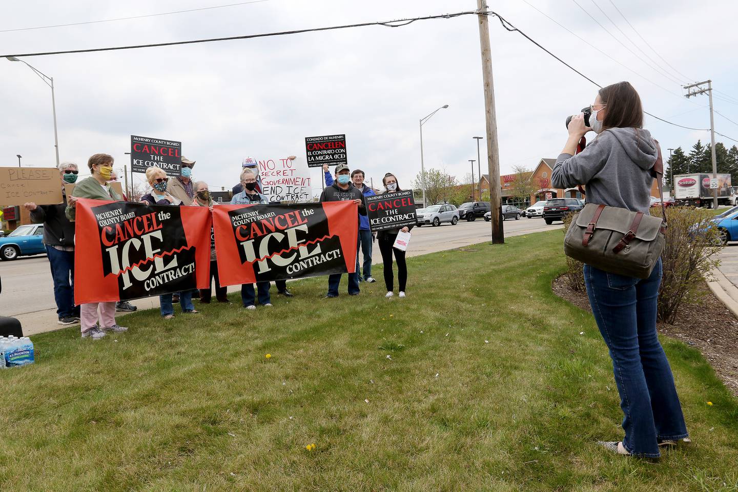Amanda Hall, right, takes a group photo of a dozen other demonstrators holding signs in favor of canceling the county's contract with U.S. Immigration and Customs Enforcement during a rally at the intersection of Front and West Elm streets on Saturday, April 24, 2021, in McHenry.