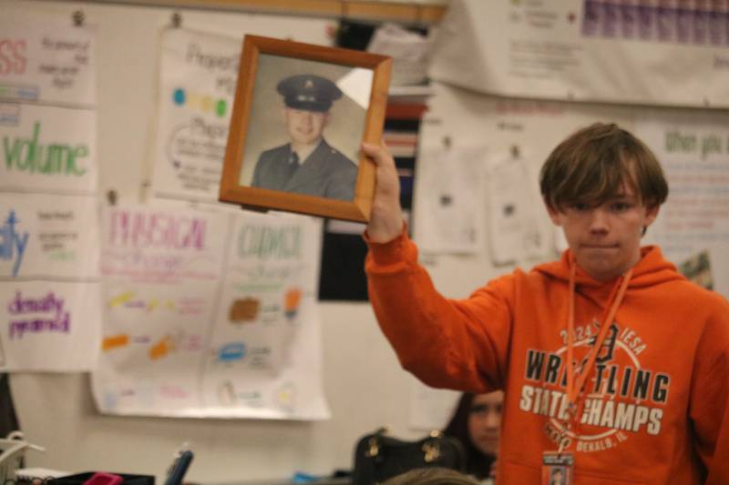 Clinton Rosette Middle School student George Russell turns and displays a photograph of Edward Higgins on Monday, Nov. 10, 2025, to some of his peers at Clinton Rosette Middle School in DeKalb. Higgins is a Vietnam War veteran from Rockford.
