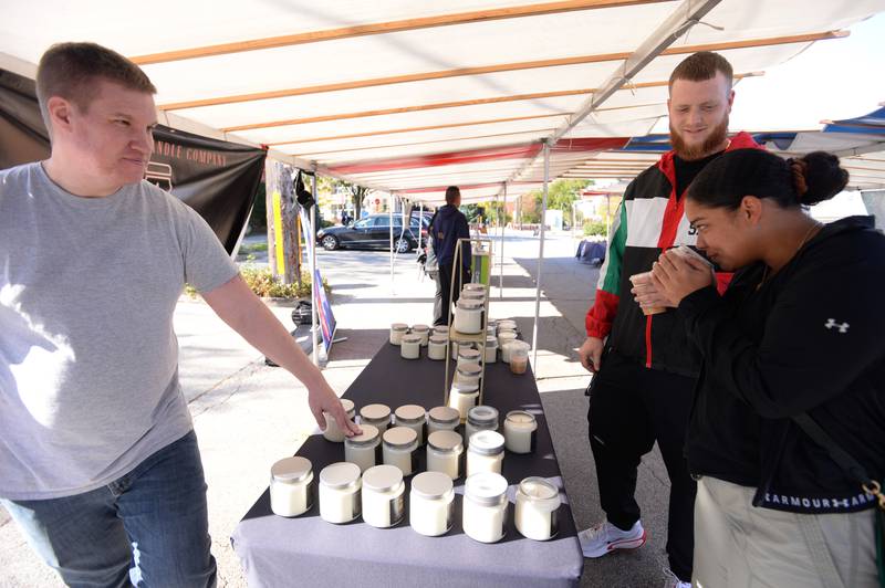 Jeff Metrick of Chicago sells candles to people including David Lobmier and Destiny Buie of Berwyn during the last day of the Glen Ellyn French Market Sunday, Oct. 20, 2024.