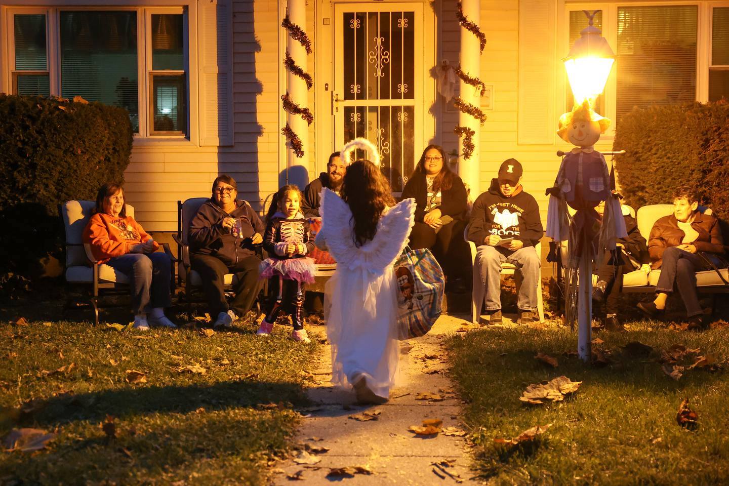 A child dressed as an angel approaches the Bradley home of Jean Tanner, left, as her neighbor, Madonna Bertrand, second from left, gather with friends and family to greet trick-or-treaters on Friday, Oct. 31, 2025.