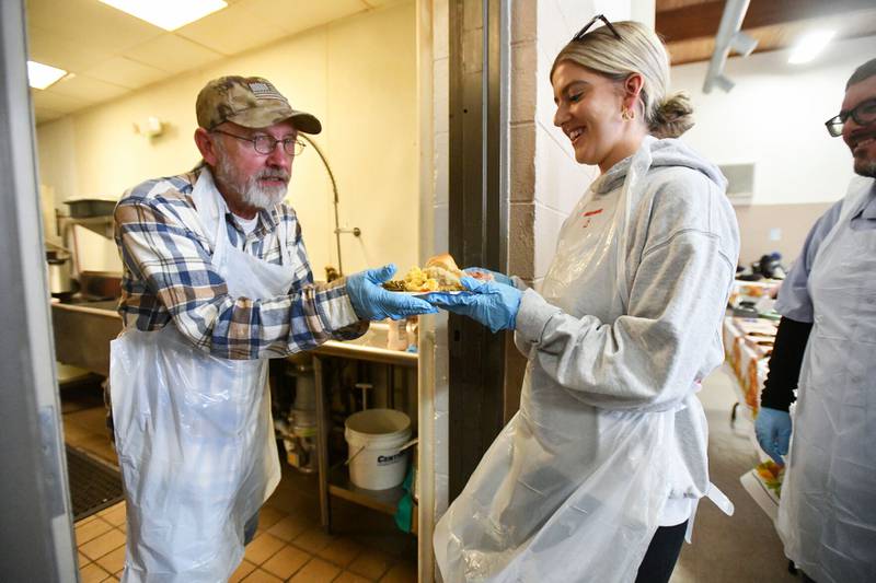 Chuck Carnes, left, hands off a plate of food to fellow volunteer Sophia Murakas, of Bourbonnais, on Wednesday during the Kankakee Salvation Army's annual Thanksgiving meal.