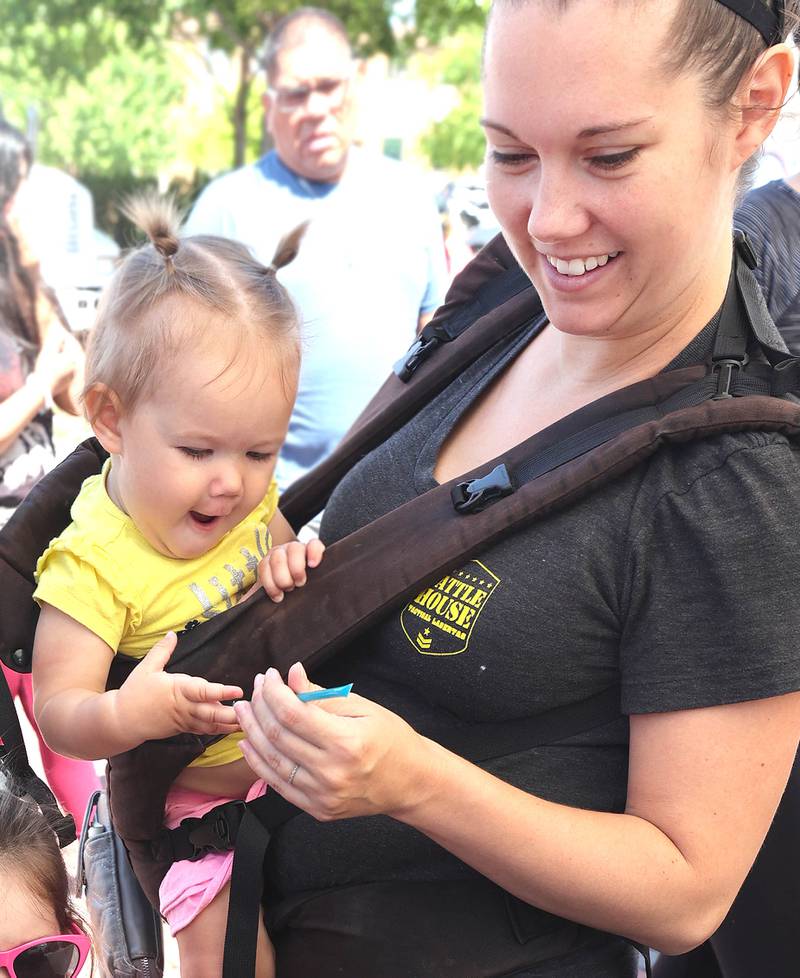 Mia Claar, 1, from DeKalb, is excited about the flavored honey stick her mom Julie got her from the Willow Creek Honey booth Thursday, June 2, 2022, during the first DeKalb Farmers Market of the season at Van Buer Plaza in Downtown DeKalb.