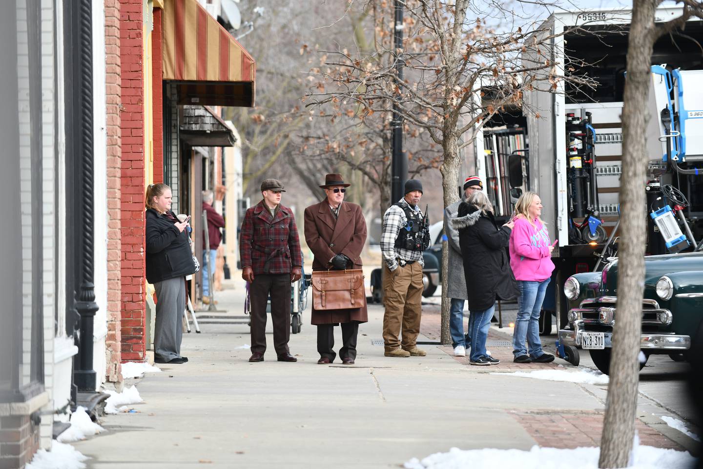 Actors in period clothing wait for their cue as bystanders watch the filming of Netflix's Monster series on Feb. 11, 2025 in downtown Momence.