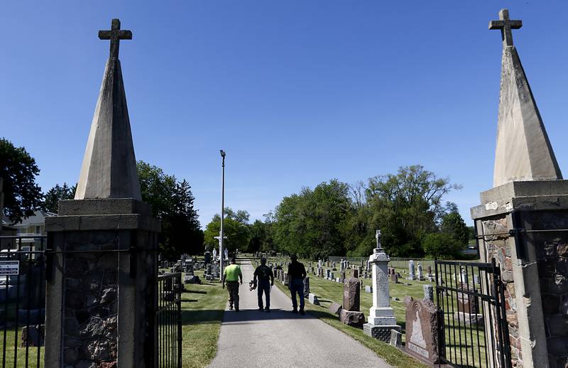 Volunteers Steve Huff, Jim Gerlick, and Jack Warneke walk into St. John the Baptist Cemetery, on Friday, May 26, 2023, as they place flags  at the graves of over 150 veterans in the cemetery, in Johnsburg.