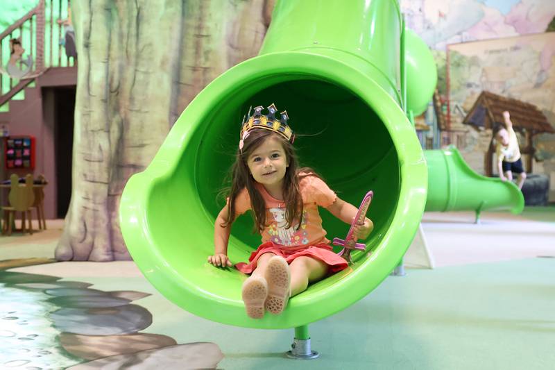 Isla Beard, 4, of Bourbonnais, arrives at the bottom of a slide with a crown and sword in hand at the Exploration Station's new Storybook Forest exhibit on Monday, June 23, 2025, during its grand opening event.