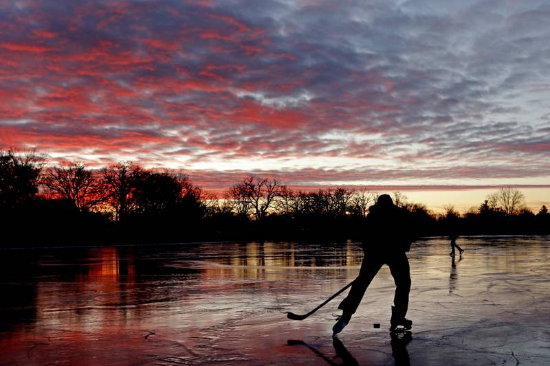 River Hudon and his dad, Rick, skate and pass a hockey puck around while playing hockey on Wednesday, Jan. 8, 2025, on Crystal Lake near West Park.
