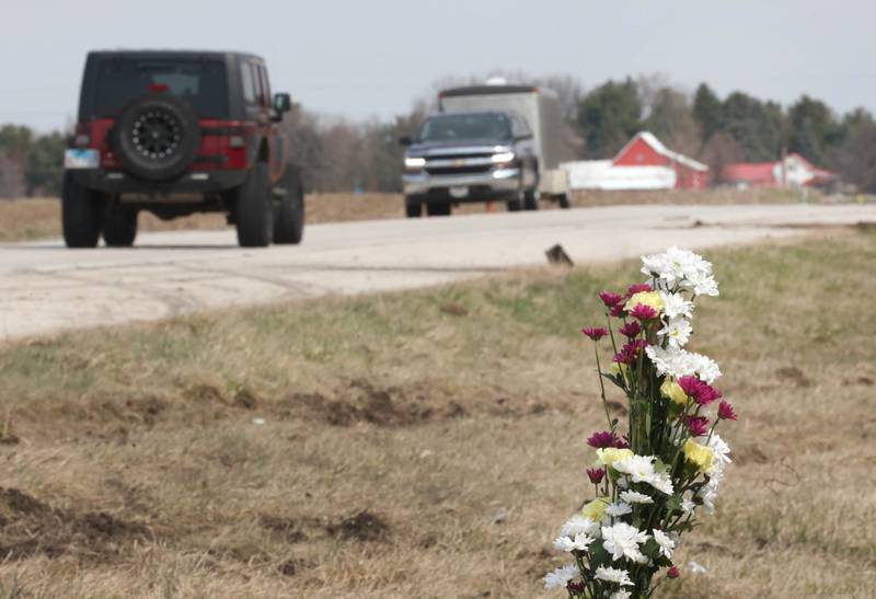 Ruts in the grass and skid marks can be seen near a memorial Friday, March 29, 2024, as traffic rolls by the site on Route 23 three-quarters of a mile south Perry Road, near DeKalb where DeKalb County Sheriff’s Deputy Christina Musil, 35, died in a crash while working a shift Thursday night.