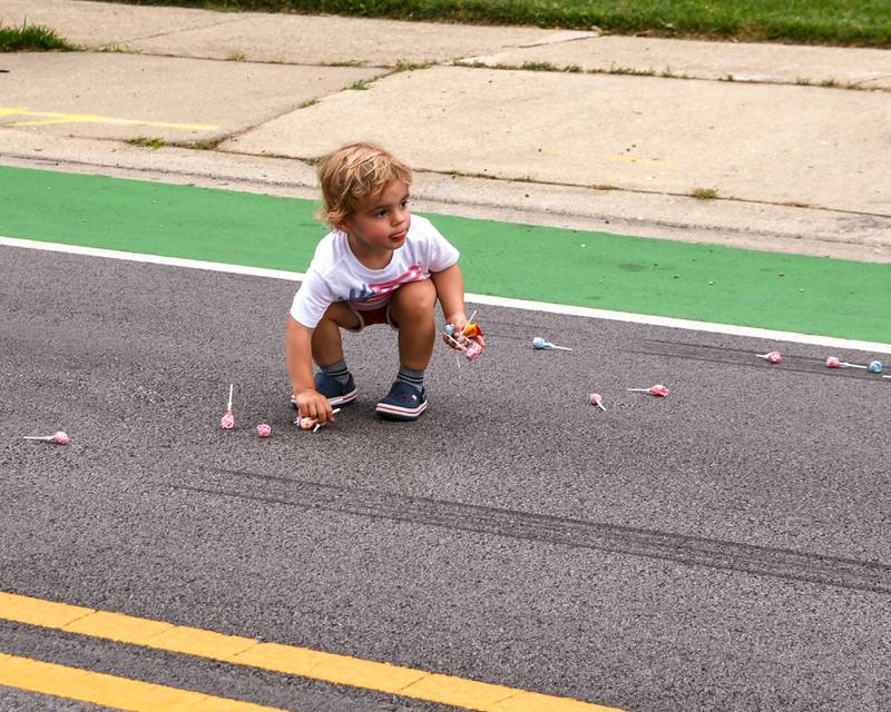 Charlie Kennedy, 2, of Downers Grove checks his surroundings as he picks up all the suckers that were thrown towards him during the Independence Day parade on Friday July 4, 2025, held in downtown Downers Grove.