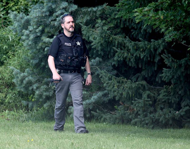 A DeKalb police officer walks the tree line Monday, July 28, 2025, that obscures a pond along the property on Ridge Drive between Sunflower Drive and Pickwick Lane where the body of an apparent drowning victim was recovered Sunday night after water rescue efforts.