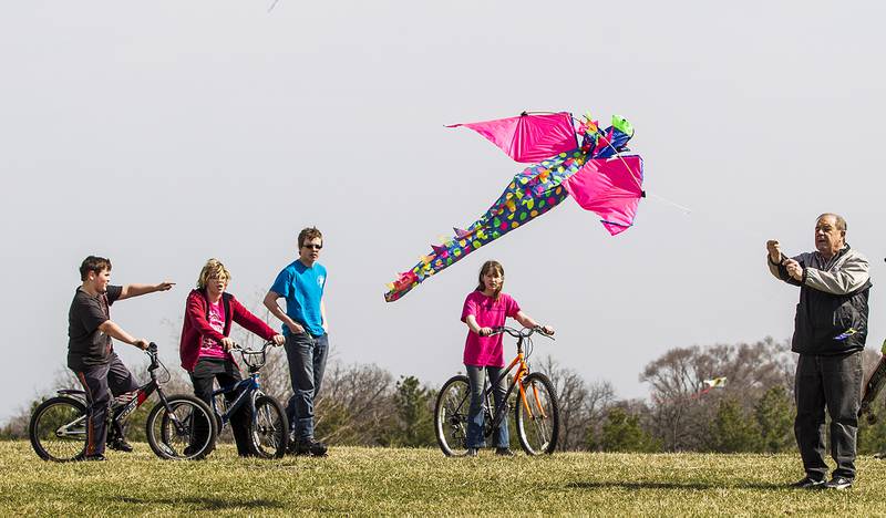 Children watch as Jim Graziano of Cary (right) flies a kite Saturday, April 19, 2014, while celebrating national kite flying month at Lions Park in Cary.