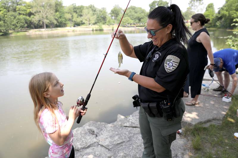 DuPage County Forest Preserve District Officer Kim Eversole helps Emma Baugh, 8, with the fish she caught during the Wheaton Police Department and DuPage County Forest Preserve Police Cops & Bobbers community fishing event at Herrick Lake Forest Preserve in Wheaton on Wednesday, June 7, 2023.