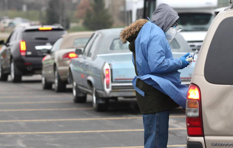 Adebayo Adeniyan, a phlebotomist from HR Support, gets information from a patron on a cold Tuesday afternoon as cars line up at the COVID-19 testing location in the parking lot at the Kishwaukee Family YMCA in Sycamore.