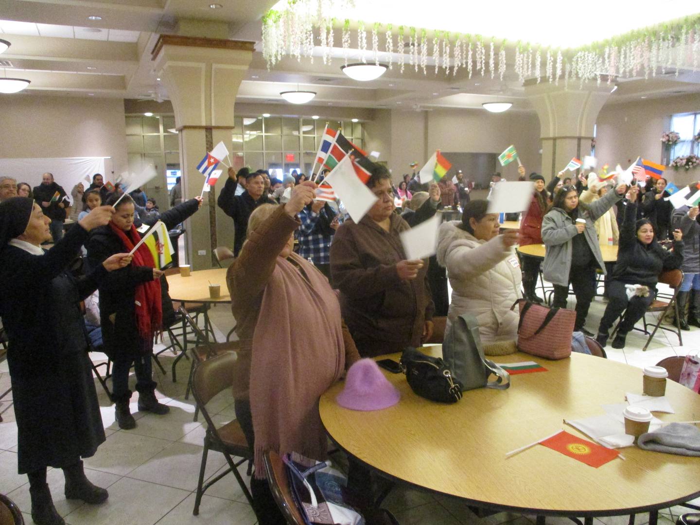 People attending a service before a truck pilgrimage wave flags of the world to show support for immigrants during a service in the hall of Our Lady of Mount Church on Jackson Street in Joliet on Saturday. Nov. 29, 2025