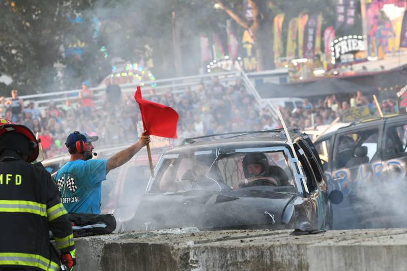 A track official uses the red flag to temporarily stop the action during the mini-van division at the 2021 demolition derby at the Whiteside County Fair. Morrison firefighters quickly extinguished the fire and the event continued to a the delight of the crowd.
