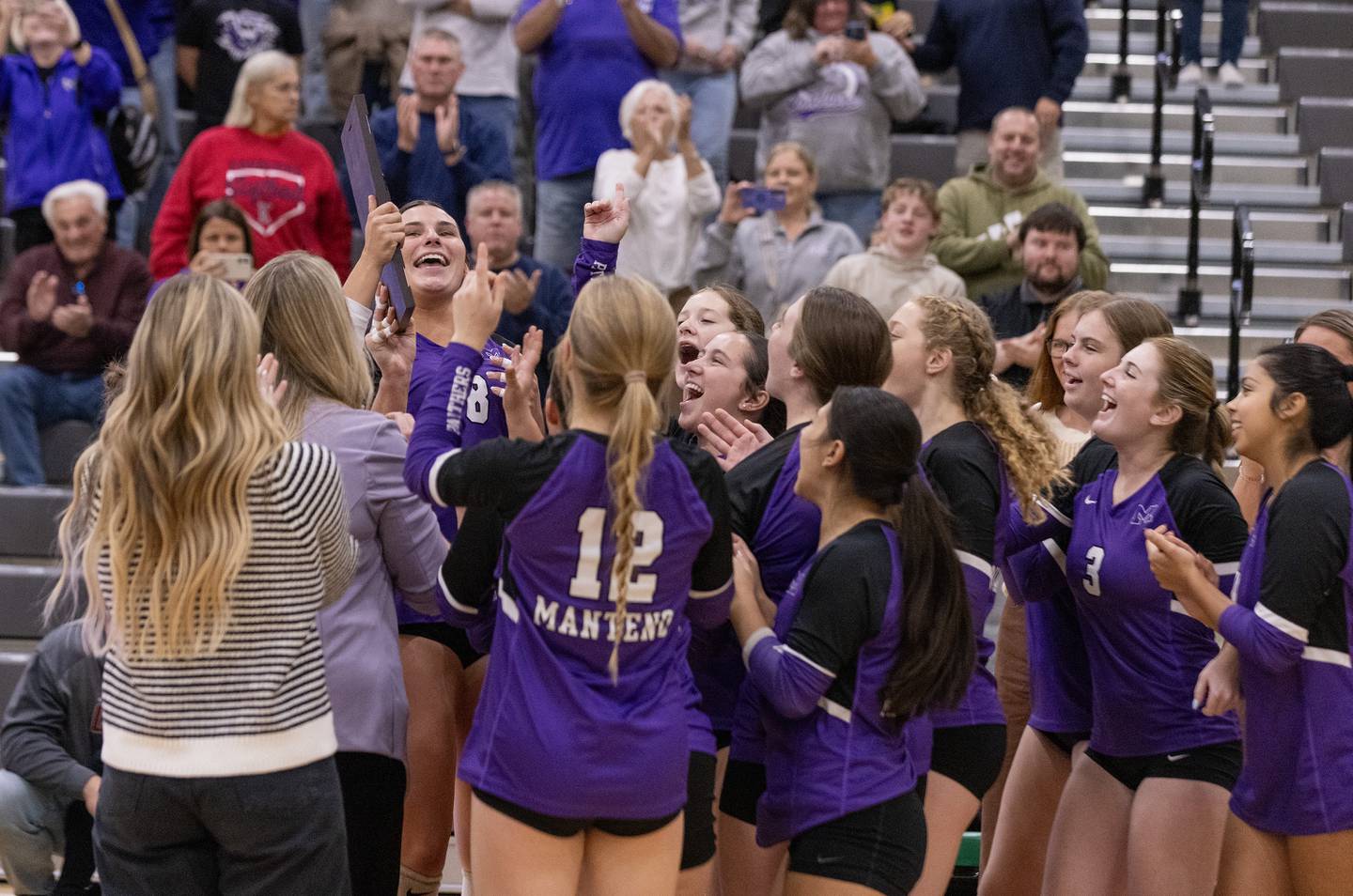 Members of the Manteno volleyball team hoist the plaque awarded to the class 2A Regional plaque as teammates cheer on Thursday, Oct. 30, 2025 at Seneca High School.