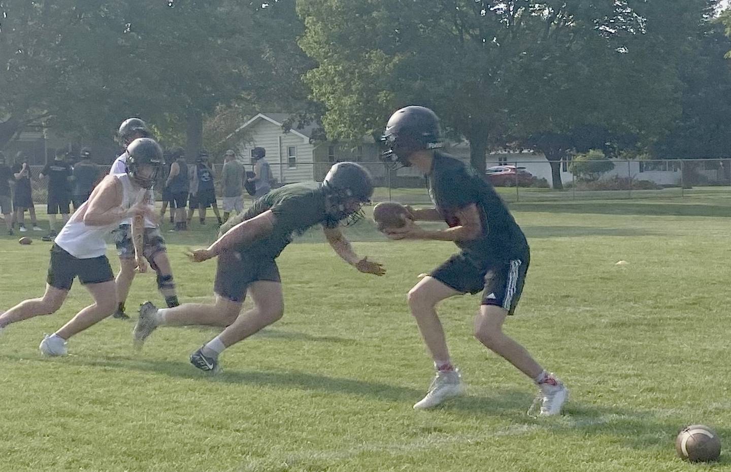 FCW quarterback Seth Jones (at right) turns to give a handoff as running backs Kesler Collins (middle) and Payton Quaintance (at left) approach the line during practice Monday, July 24, 2023.