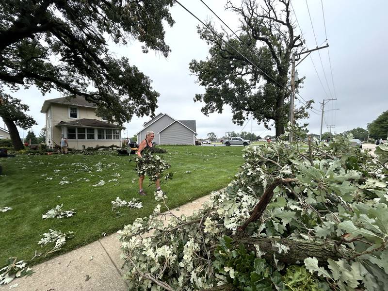 Jan Cox carries storm debris to the curb as she and others work at her home on 1113 W. Second Street in Byron on Tuesday, July 16, 2024.