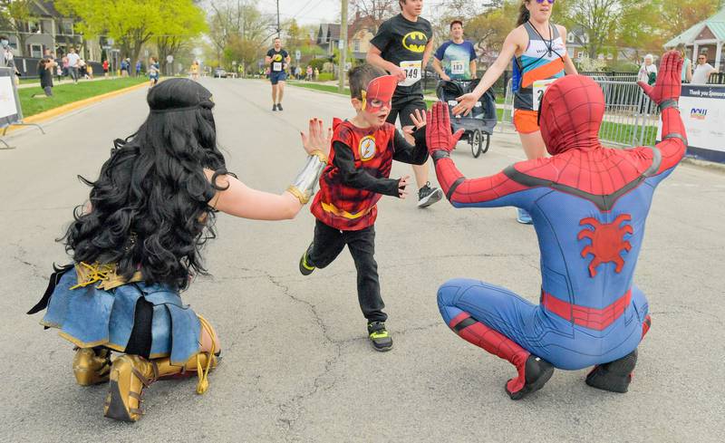 Liam Roemer, 5 of Wheaton hi-fives Wonder Woman and Spiderman as he crosses the finish line of the Super Hero 5k Fun Run in Wheaton on Saturday, April 15, 2023.