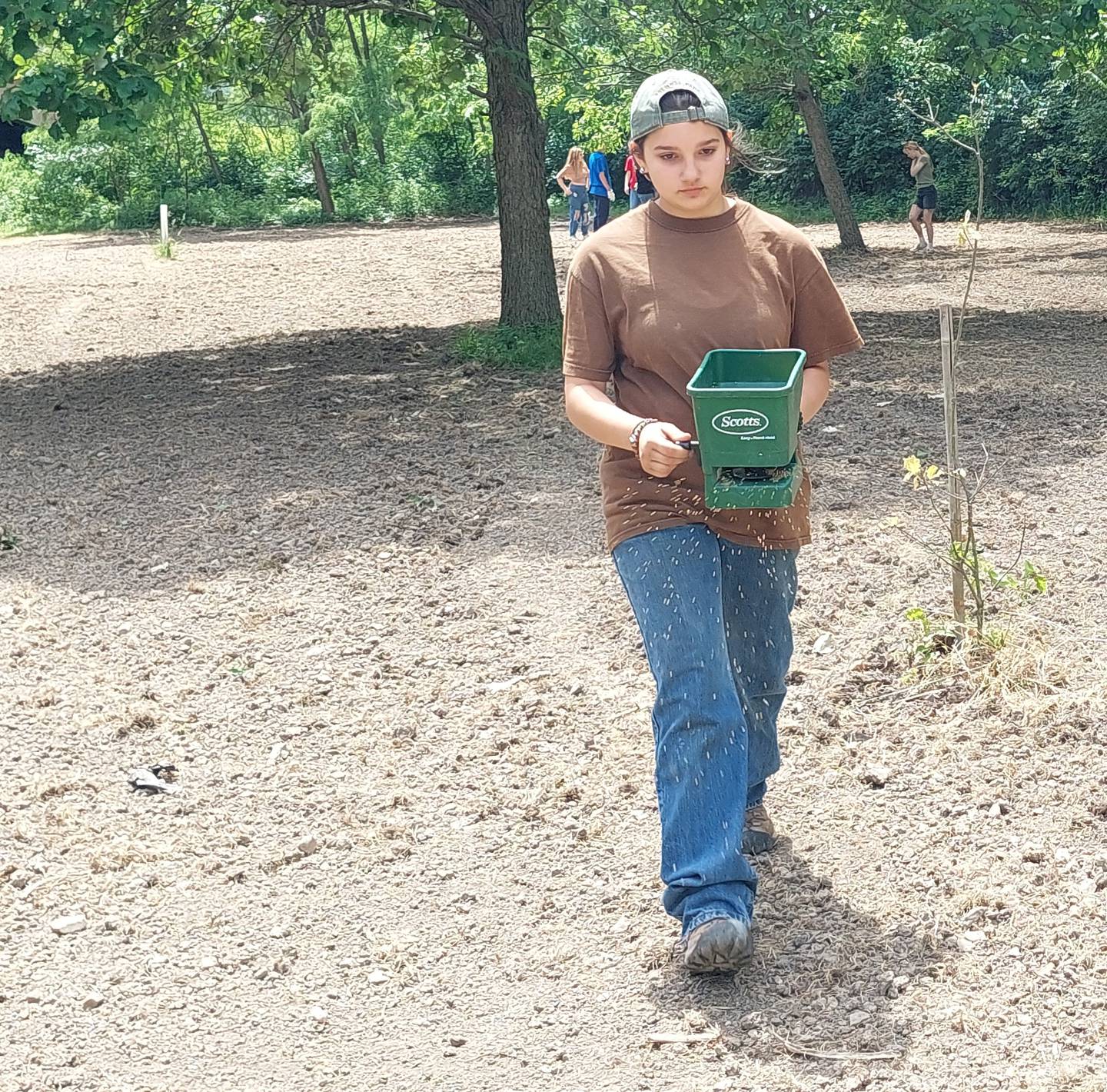 Milton Pope eighth grader Sophia Swift spreads seed Wednesday, May 22, 2024, into a sunflower and red millet plot at Illini State Park.